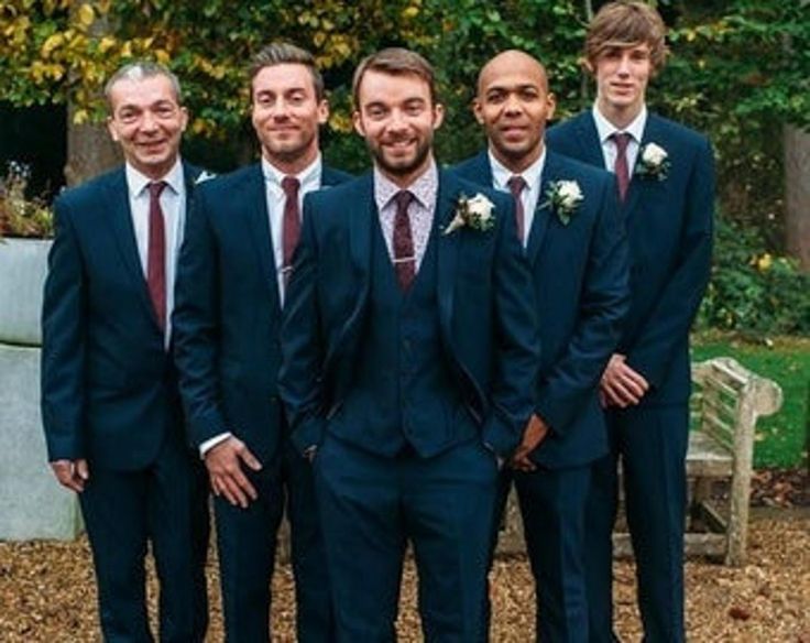 a group of men standing next to each other wearing suits and ties with flowers on their lapels