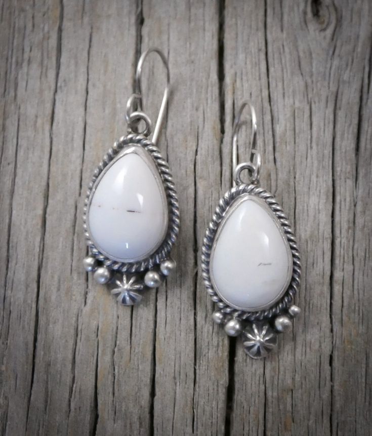 100% handcrafted from Sterling Silver and White Buffalo; Navajo Native American silversmiths are recognized among the finest in the world. This work of art features striking, rare, White Buffalo stones. This stunning semi precious gemstone is smooth white in color and is marked with a touch of black matrix. This is that go to accessory that you can wear often due to the neutral nature of the stones and will quickly become your signature! Measures: 1 1/2" x 9/16" (with ear wires) 10 grams Stamped Artisan White Jewelry Stamped 925, Artisan Teardrop Jewelry Stamped 925, White Artisan Jewelry Nickel Free, Artisan White Sterling Silver Jewelry, Artisan Teardrop-shaped Sterling Silver Jewelry, Southwestern Teardrop Gemstone Jewelry, Southwestern Style Teardrop Gemstone Jewelry, Unique White Sterling Silver Jewelry, White Artisan Earrings For Pierced Ears