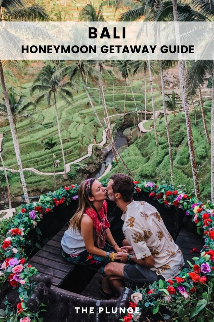 a man and woman sitting on top of a wooden bridge surrounded by lush green trees