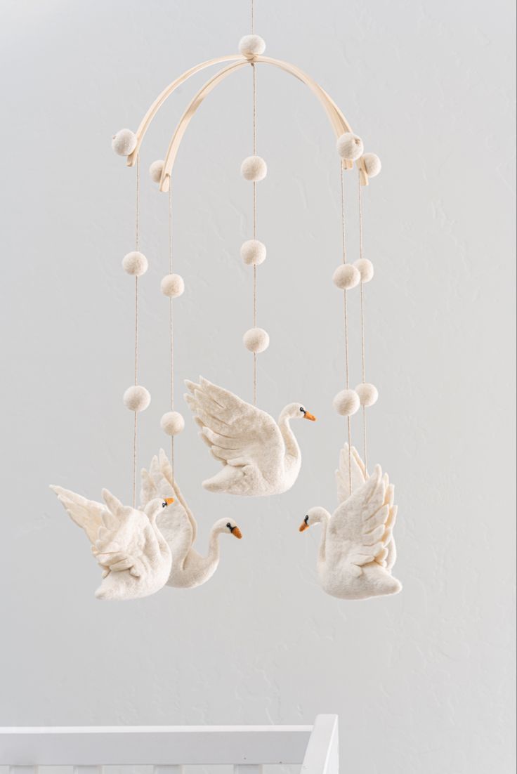 three white birds hanging from a mobile with balls