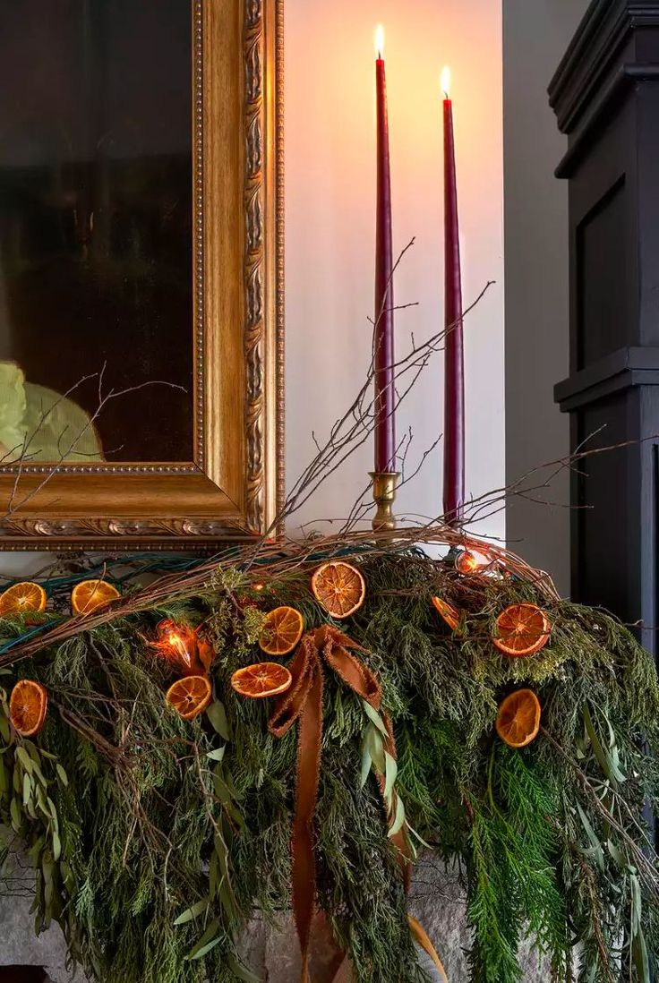 an arrangement of oranges and greenery on a mantle with candles in the background