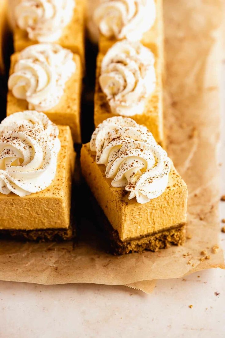 several slices of pumpkin cheesecake with whipped cream on top, sitting on parchment paper