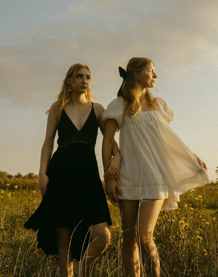 two young women walking through a field holding hands