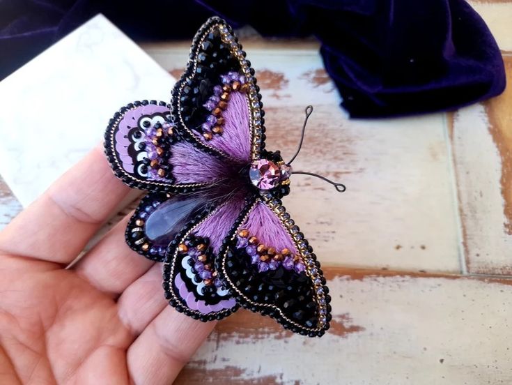 a hand holding a purple and black butterfly