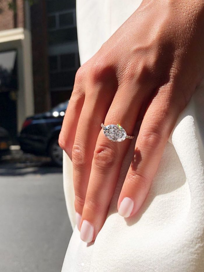 a woman's hand with a diamond ring on her finger, in front of a city street