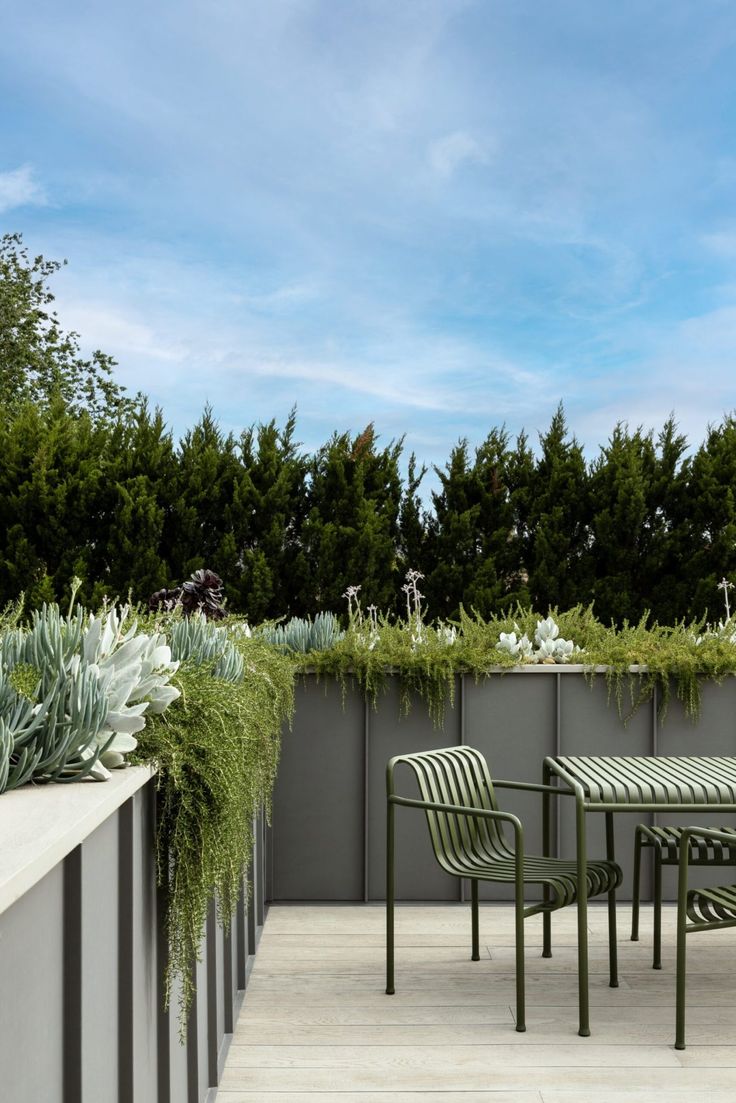 an outdoor table and chairs with plants growing on the wall next to it, in front of a blue sky