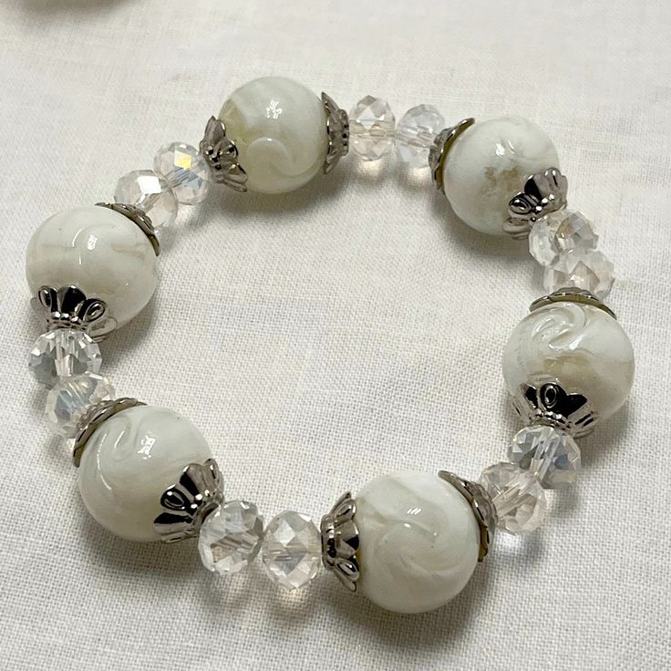 Handmade Stretch Bracelet With Large White Marble Beads And Smaller, Iridescent Beads And Silver Accents White Pearl Stretch Bracelet For Party, Elegant White Beaded Stretch Bracelet, Elegant White Beaded Crystal Bracelet, Adjustable Beaded Stretch Bracelet In Pearl White, Elegant Stretch Bracelet With Colorful Beads, Adjustable Pearl White Beaded Stretch Bracelet, Adjustable White Beaded Pearl Bracelet, Elegant White Crystal Bracelet With Spacer Beads, White Stretch Bracelet With Colorful Beads