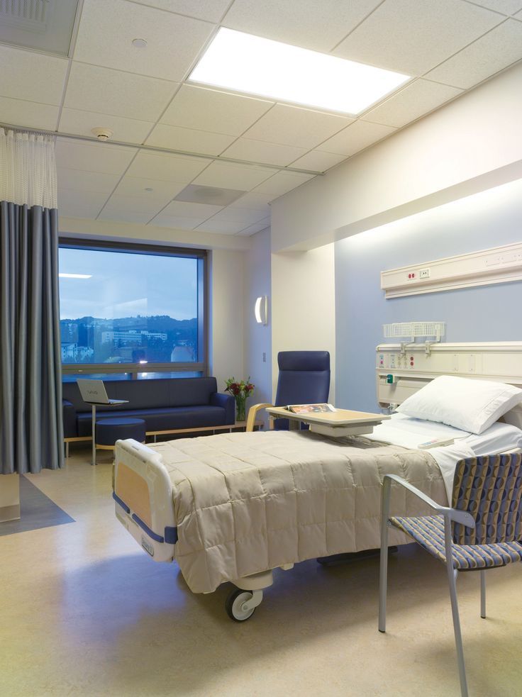 an empty hospital room with a bed and chairs