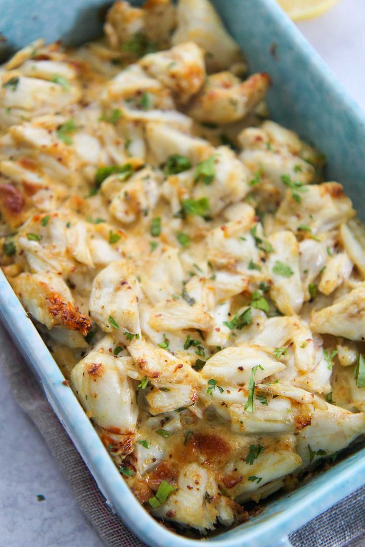 a casserole dish with chicken and cheese in a blue baking dish next to a lemon wedge