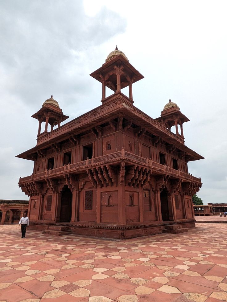 a large wooden building sitting on top of a stone floor next to a person standing in front of it