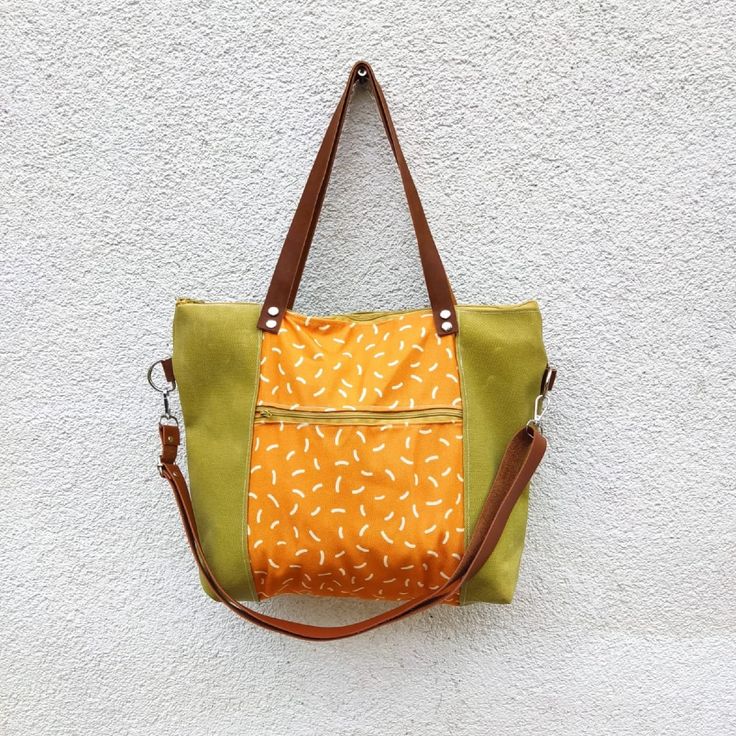 an orange and green handbag hanging on a white wall next to a brown leather strap