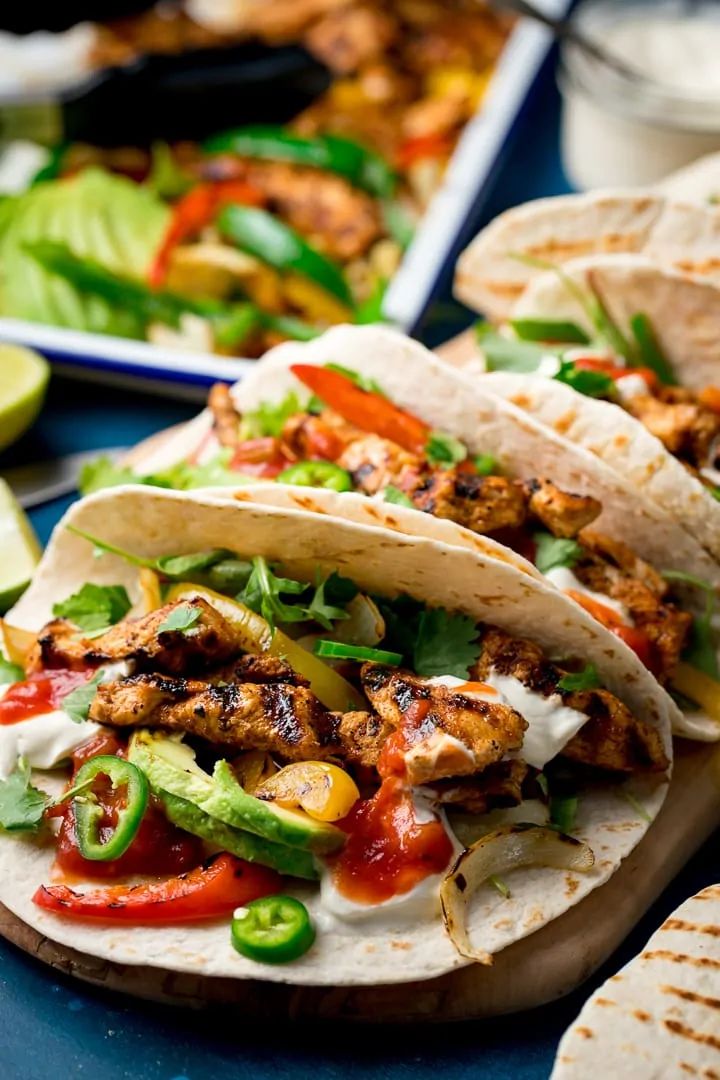 three tacos with chicken, peppers, and avocado on a blue plate