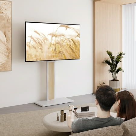 two people sitting on a couch in front of a flat screen tv with an abstract painting behind them