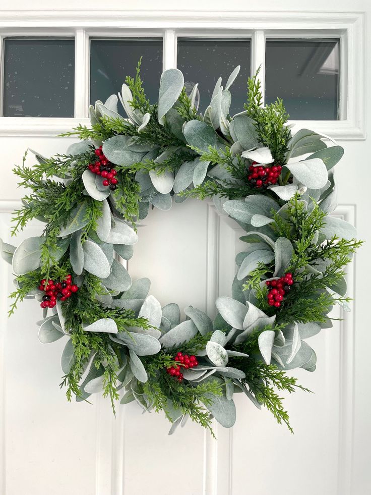 a christmas wreath hanging on the front door with holly and red berries, greenery and mist