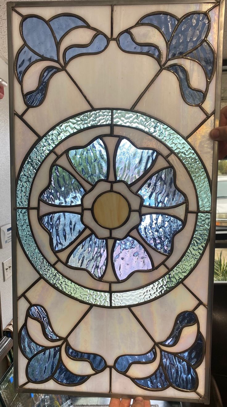 a person holding up a stained glass window with blue and green designs on the side