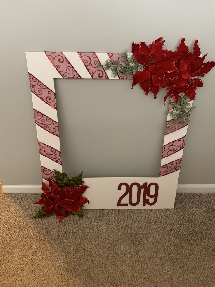 a white frame decorated with red poinsettis and ribbon on carpeted floor