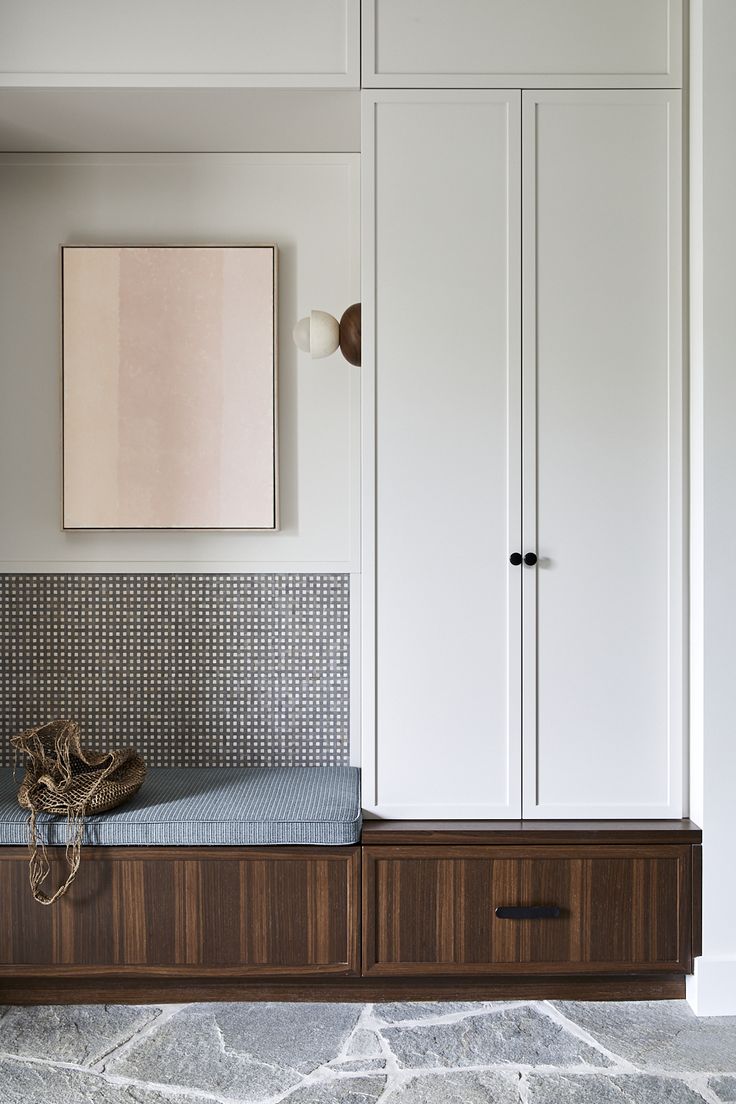 a wooden bench sitting in front of a white closet with a painting on the wall