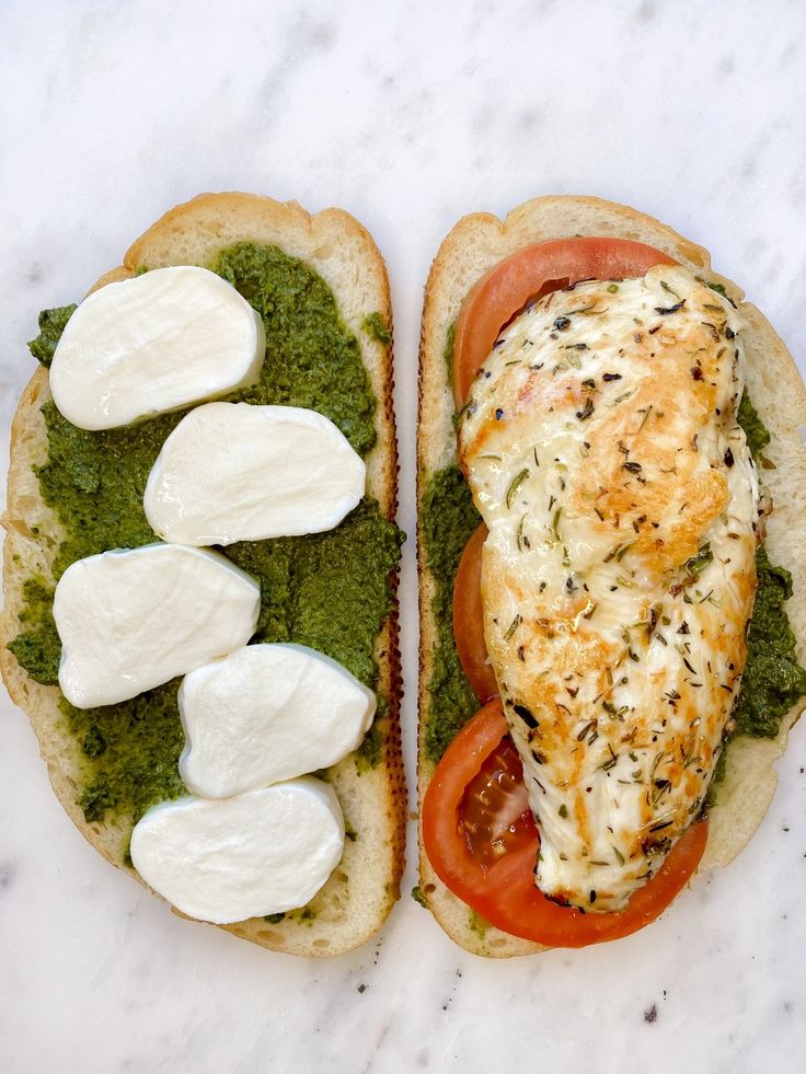 two sandwiches with cheese, tomatoes and pesto on them sitting on a marble surface