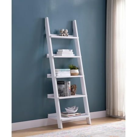 a white leaning shelf with books on it in front of a blue wall and rug