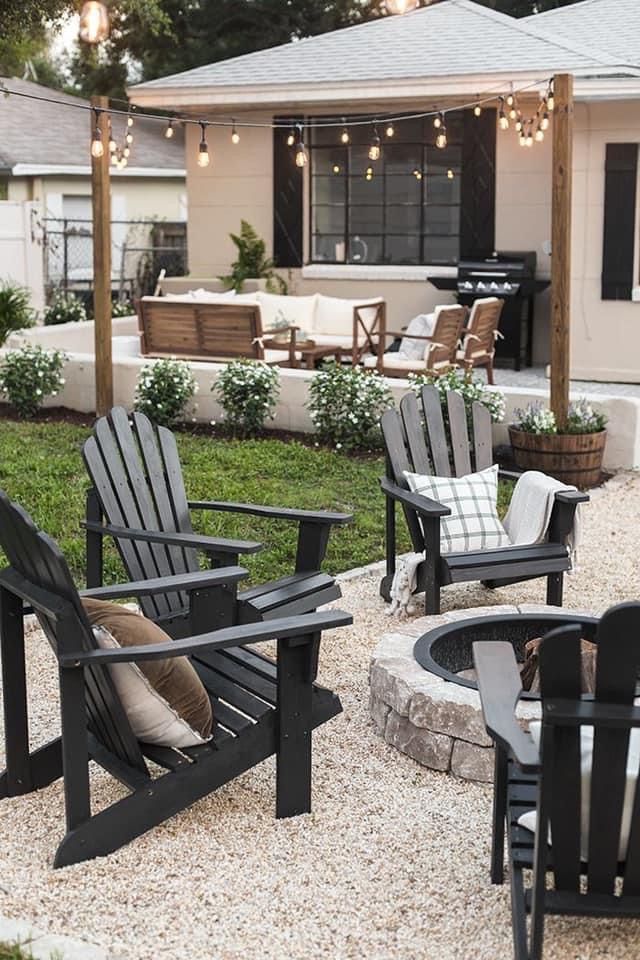 an outdoor patio with chairs, fire pit and grill area in the back yard is lit by string lights