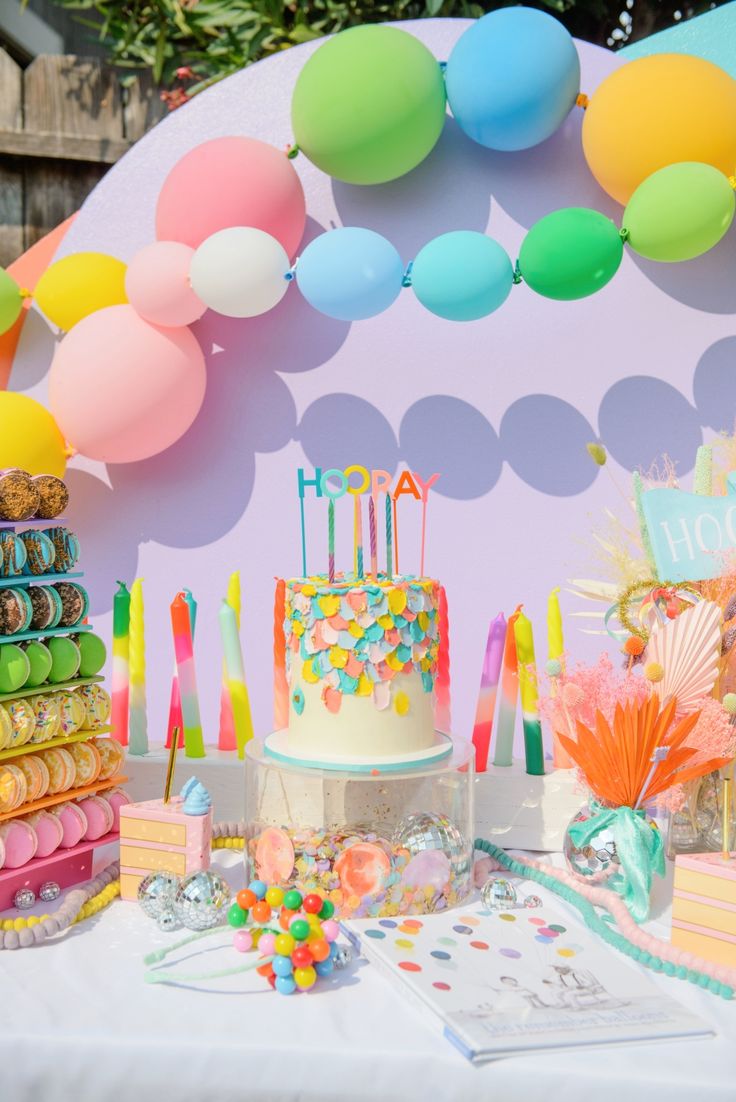 there is a birthday cake on the table with balloons and confetti around it