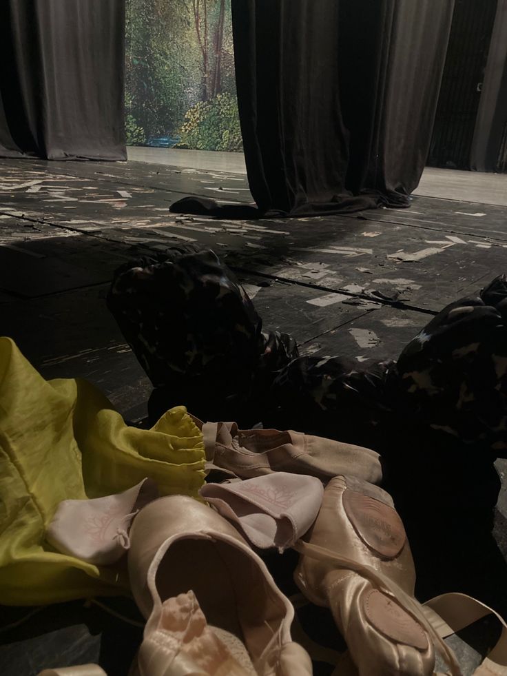 several pairs of ballet shoes sitting on the floor in front of black curtained windows