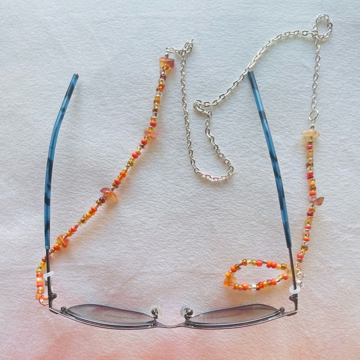 Elegant Beaded Eyeglass Chain Sunglass Strap Unisex Eyeglass Holder Reading Retainer Strap Silver Toned Chain Orange Fine Seed Beads & Chips Length: 29.5in Versatile Eyeglasses Chains: Which Are Suitable For Sunglasses, Reading Glasses, Masks And So On. These Gorgeous Beaded Eyeglass Chains Prevent Your Glasses From Getting Lost. Lightweight Material: These Elegant Eyewear Retainer Chains And Beads Are Made Of High Quality Materials. Handcrafted By Norclar Custom-Made Jewelry & Accessories Beaded Clear Glass Glasses Chains, Clear Beaded Glass Glasses Chains, Silver Glass Jewelry For Festival, Silver Beaded Glass Chain For Glasses, Silver Beaded Glasses Chains For Beach, Silver Glass Beaded Necklace With Colorful Beads, Silver Beaded Necklace With Colorful Glass Beads, Silver Glass Jewelry With Colorful Beads, Silver Jewelry With Colorful Glass Beads