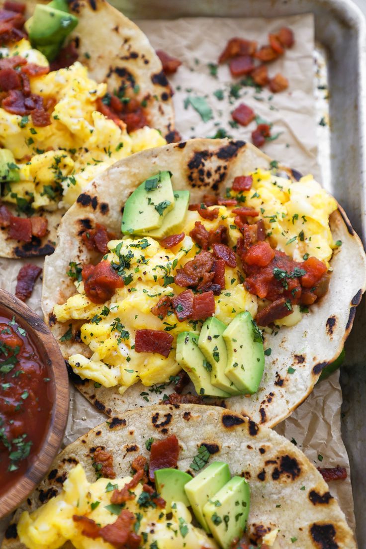 three tortillas with eggs, avocado and tomato on them in a pan