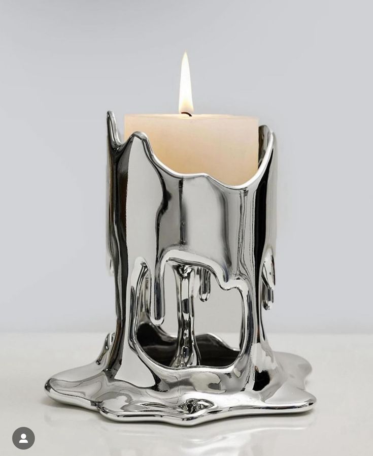 a silver candle holder with a lit candle in it's center on a white surface