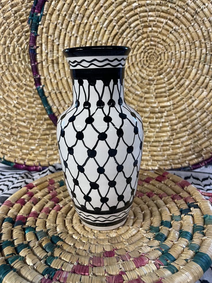 a black and white vase sitting on top of a woven place mat next to straw baskets