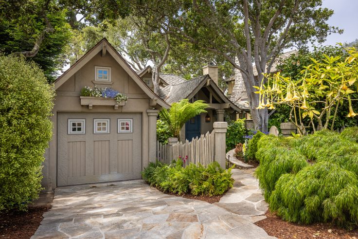 a small house surrounded by lush green trees and shrubbery in front of it is a stone path leading to the entrance