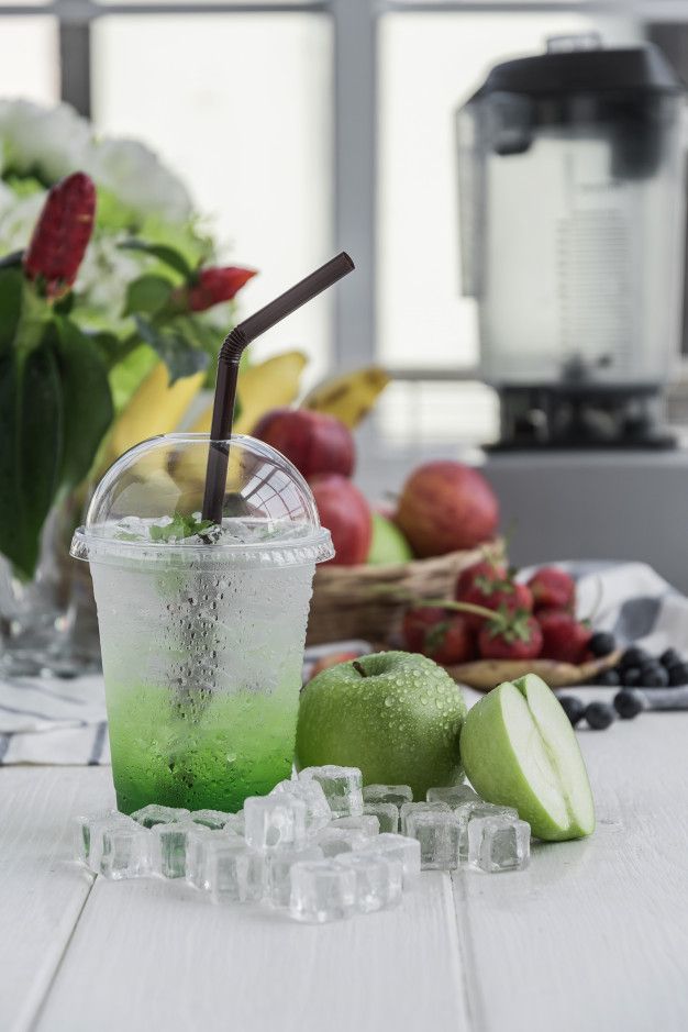 a green drink sitting on top of ice next to fruit