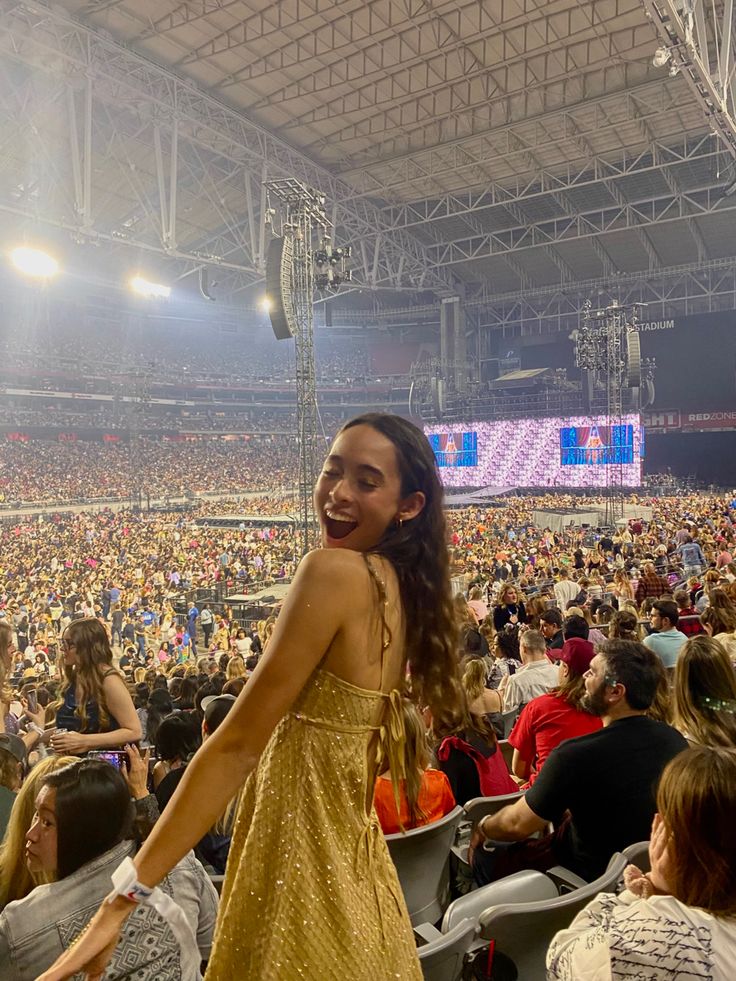 a woman standing in front of a large crowd at a sporting event, wearing a gold dress