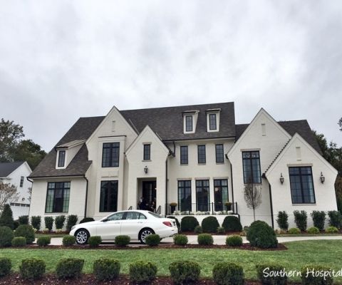 a white car is parked in front of a large house with hedges and bushes around it