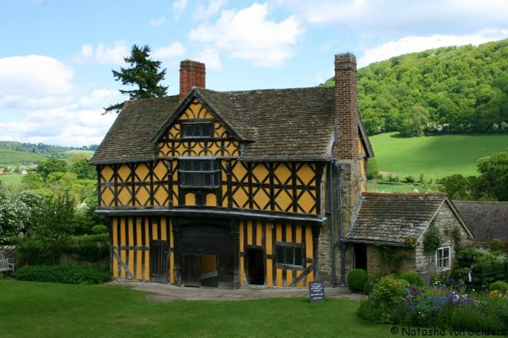 an old house with yellow and black stripes on it's walls, surrounded by lush green fields