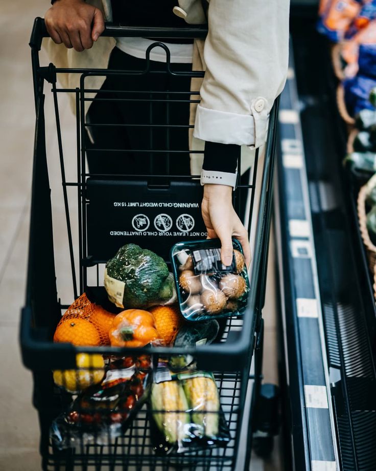 a person pushing a shopping cart filled with fruits and vegetables