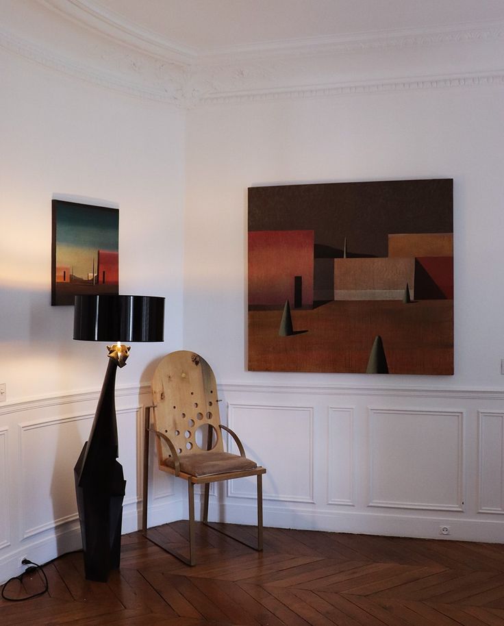 a room with a chair, lamp and paintings on the wall