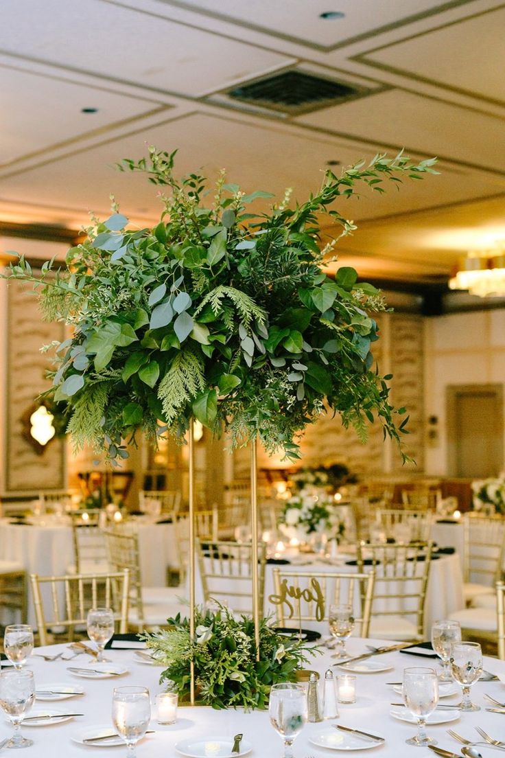 a tall centerpiece with greenery sits on top of a table