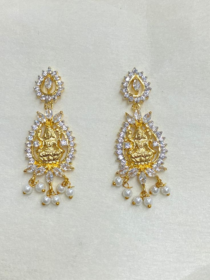 Welcome to Ray Fineornates Jewellery, where Divine Opulence meets exquisite craftsmanship! Our Gold Plated Temple Earring Set featuring the iconic South Indian Lakshmi design is a true reflection of timeless beauty and tradition. These earrings are meticulously crafted with 22k yellow gold plating, capturing the essence of authentic Temple jewellery. The intricate Lakshmi Ji design showcases the goddess of wealth and prosperity, symbolizing divine blessings and grace. At Ray Fineornates Jeweller Gold Earrings For Puja, Elegant Earrings For Diwali Puja, Dangle Latkans Earrings For Puja, Elegant Earrings For Puja And Diwali, Elegant Latkans Earrings For Puja, Latkan Dangle Earrings For Puja, Gold Jewelry With Matching Earrings For Navratri, Elegant Danglers For Puja, Temple Jewelry Style Bridal Earrings