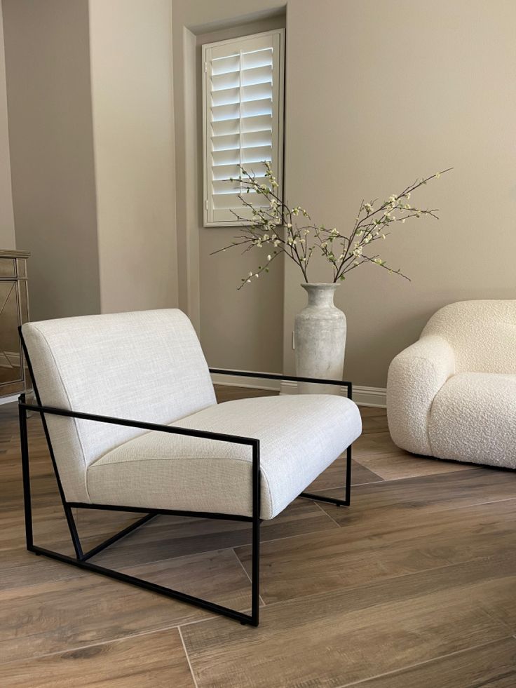 a white chair sitting next to a vase with flowers in it on top of a hard wood floor