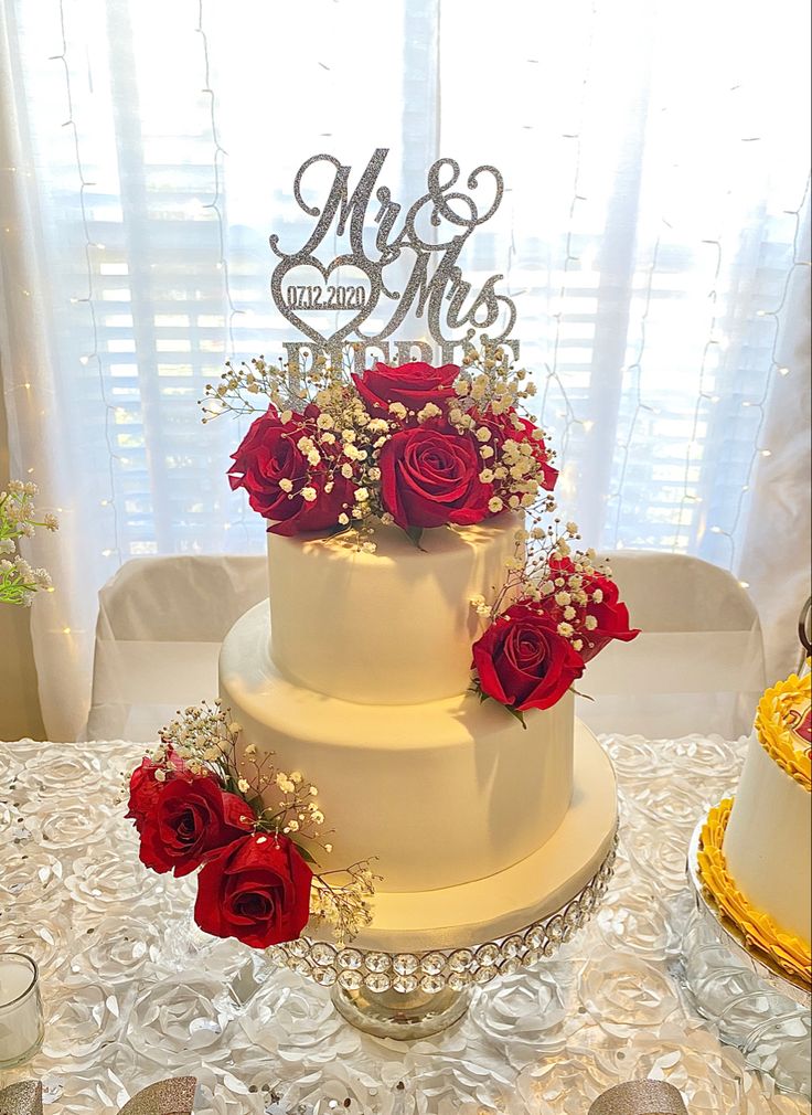 a three tiered wedding cake with red roses on the side and mr and mrs topper