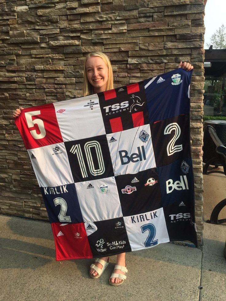 a woman holding up a soccer jersey in front of a stone wall