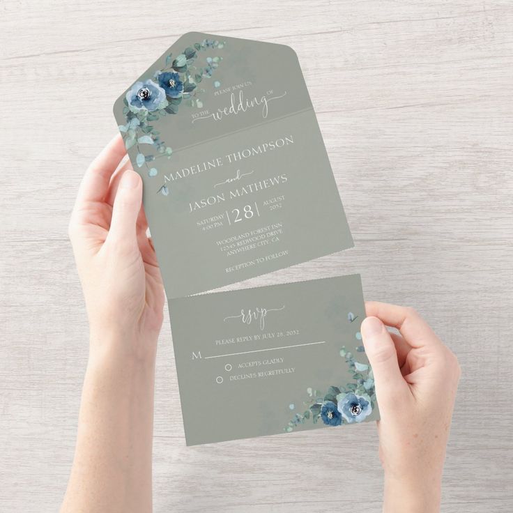 someone holding up two wedding cards with blue flowers on the front and back of them