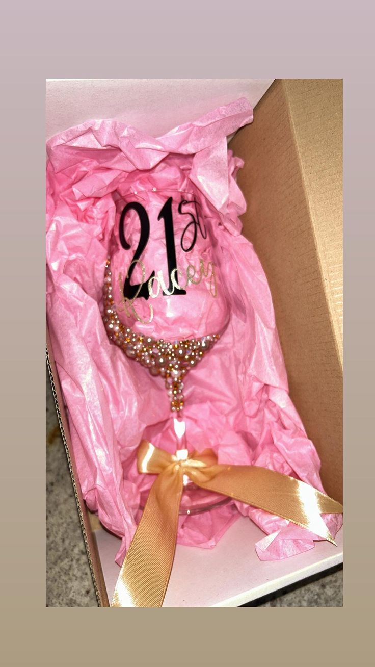 the 21st birthday cake is in a pink gift box with gold ribbon and pearls on it