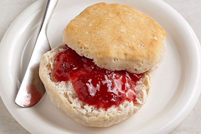 a white plate topped with a biscuit covered in strawberry jam next to a knife and fork