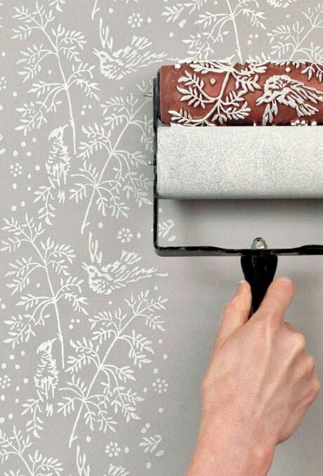 someone using a roller to paint a wall with white flowers and leaves on grey background