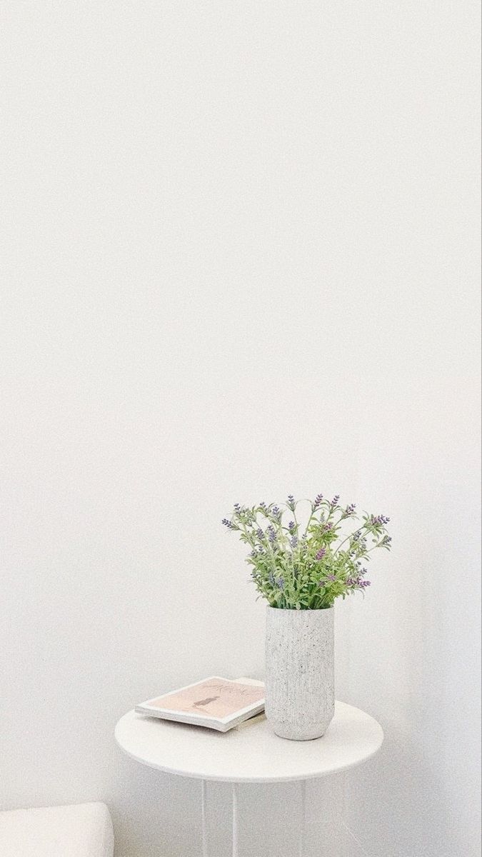 a small white table with a plant on it and a book sitting on top of it