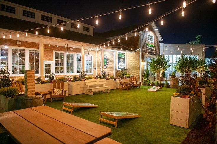 an outdoor seating area at night with lights strung over the building and lawn furniture set up