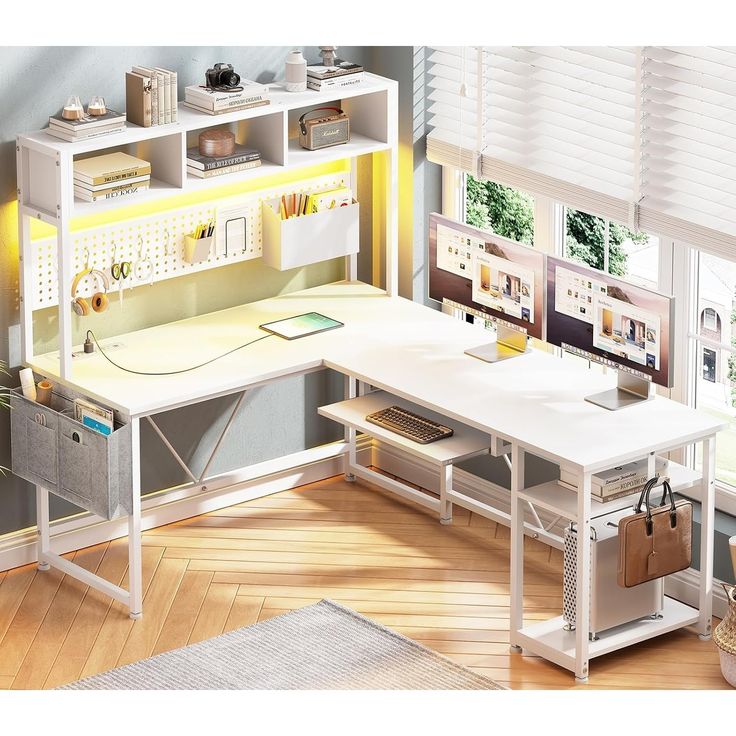 a computer desk sitting in front of a window next to a white shelf filled with books