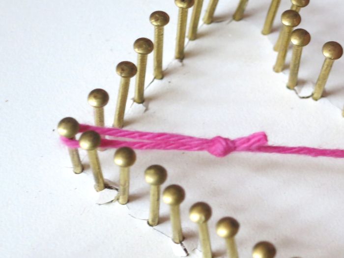 a heart made out of pins with a pink string tied around it on a white surface